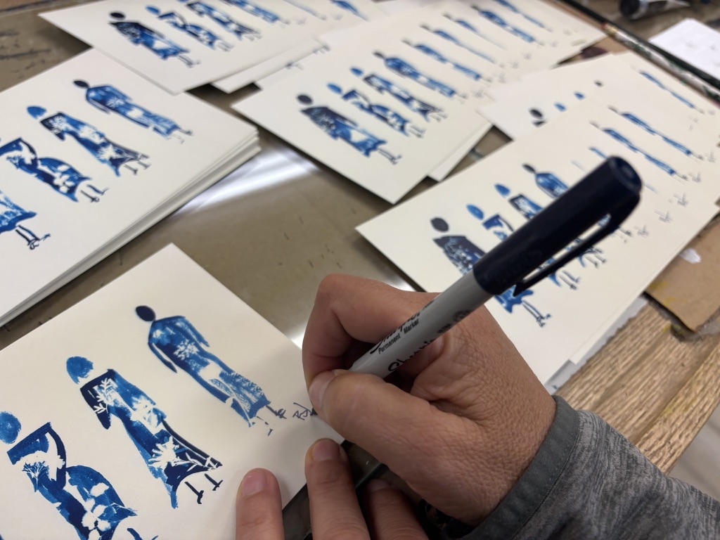 The artist signing a stack of blue cyanotype prints